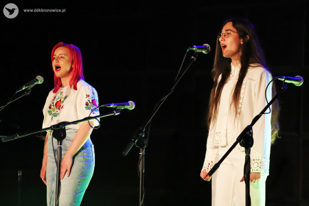 Kolorowe zdjęcie. Dwie dziewczyny śpiewają do mikrofonów na scenie.