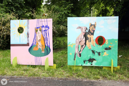 Kolorowe zdjęcie. Dwie foto-plansze do robienia zdjęć ze swoją twarzą stoją na trawie. Po prawej na planszy znajdują się psy. Po lewej na planszy znajduje się kot.