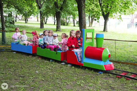 Kolorowe zdjęcie. Grupa dzieci siedzi w kolorowym pociągu na dworze.