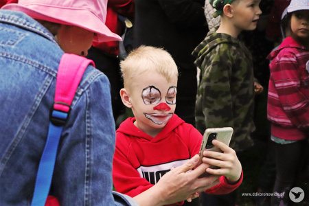 Kolorowe zdjęcie. Chłopiec z pomalowaną twarzą jak klaun robi sobie selfie telefonem.
