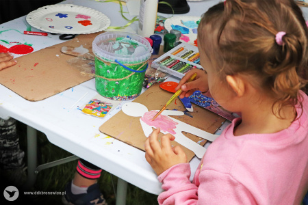 Kolorowe zdjęcie. Dziewczynka maluje farbami papierową postać ludzika.