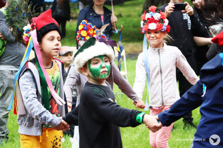 Kolorowe zdjęcie. Dzieci w ludowych czapkach i wiankach tańczą na dworze po kole trzymając się za ręce.