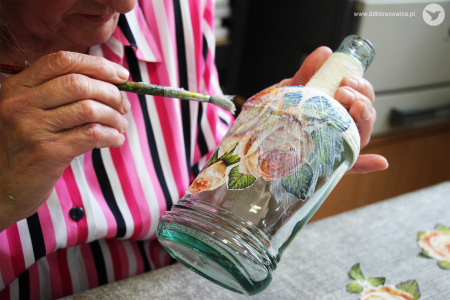Kolorowe zdjęcie. Kobieca dłoń maluje pędzlem po szklanej butelce.