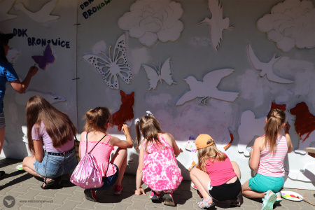Kolorowe zdjęcie. Dzieci kucają i malują wielkoformatową tablicę ze zwierzętami.
