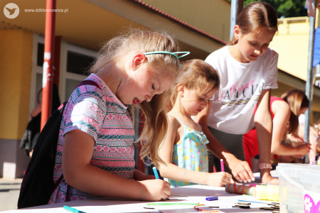 Kolorowe zdjęcie. Dziewczynki malują flamastrami drewniane zawieszki przy stoliku warsztatowym.