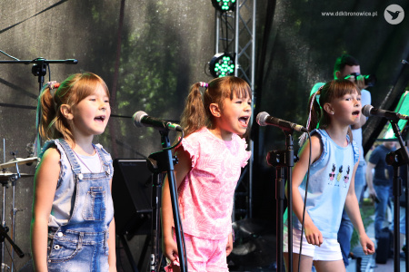 Kolorowe zdjęcie. Trzy dziewczynki śpiewają do mikrofonów na scenie.