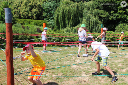 Kolorowe zdjęcie. Na dworze. Dzieci przechodzą przez labirynt stworzony za pomocą różnokolorowych sznurków.