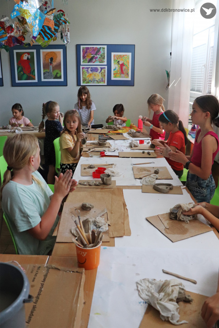 Kolorowe zdjęcie. Dzieci siedzą przy stole i robią figurki z gliny.
