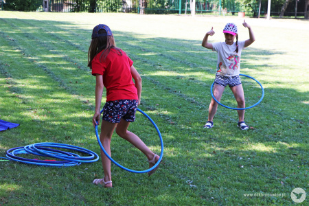 Kolorowe zdjęcie. Dwie dziewczynki bawią się hula hop na trawie.