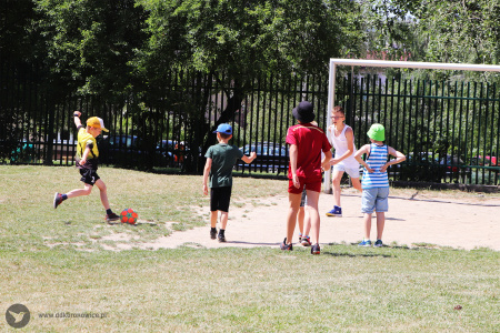 Kolorowe zdjęcie. Grupa chłopców gra w piłkę nożną na trawiastym boisku przy bramce.