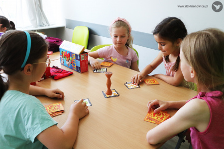 Kolorowe zdjęcie. Cztery dziewczynki siedzą przy stoliku i grają w grę planszową.