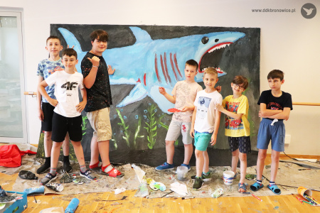 Kolorowe zdjęcie. Chłopcy pozują do zdjęcia przy wykonanym obrazie rekina.