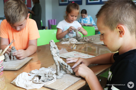 Kolorowe zdjęcie. Dzieci siedzą przy stoliku i lepią figurki z gliny.