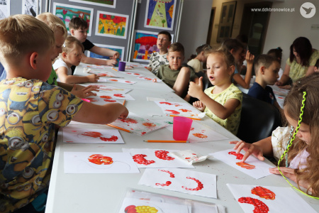 Kolorowe zdjęcie. Dzieci siedzą przy stole i malują palcami obrazy w technice petrykiwka.