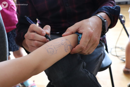 Kolorowe zdjęcie. Męskie dłonie rysują długopisem na przedramieniu dziecka kamerę.