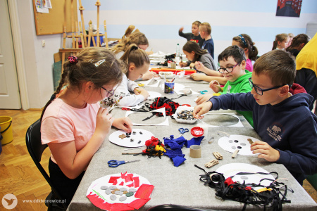 Kolorowe zdjęcie. Dzieci siedzą przy stoliku. Tworzą potwory z guzików i kolorowej bibuły.