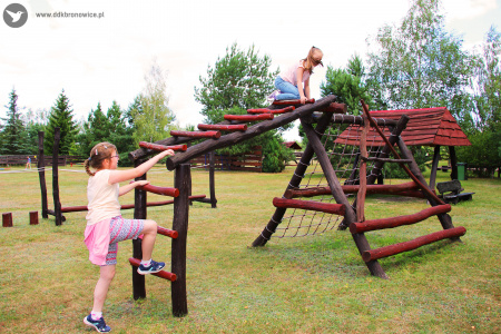 Kolorowe zdjęcie. Na dworze. Dwie dziewczynki wspinają się na drewnianych drabinkach.