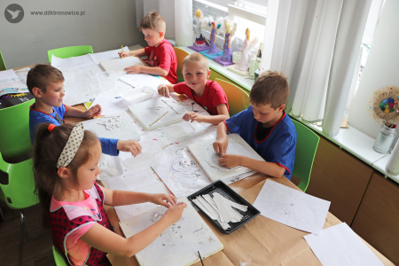 Kolorowe zdjęcie. Dzieci siedzą przy stole i pracują nad płaskorzeźbami z gipsu.