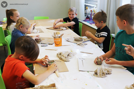 Kolorowe zdjęcie. Dzieci pracują przy stole. Robią naczynia i figurki z gliny.