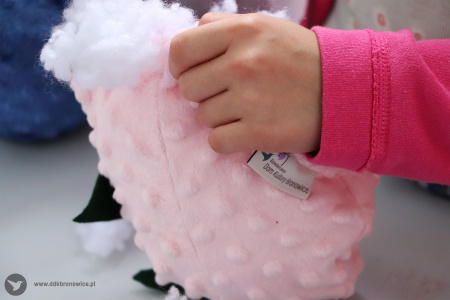Kolorowe zdjęcie. Dziecięca dłoń wypycha wypełniaczem różowego pluszaka.