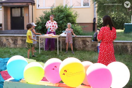 Kolorowe zdjęcie. Instruktorka DDK Bronowice prowadzi animacje z dziećmi z baniek mydlanych. Na pierwszym planie widać kolorowe balony.