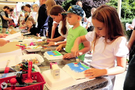 Kolorowe zdjęcie. Dzieci przy stoliku warsztatowym, malują pędzlami po styropianowych tackach.