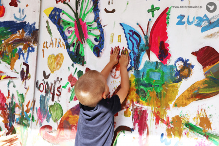Kolorowe zdjęcie. Chłopiec odbija swoje dłonie na wielkoformatowej ściance.