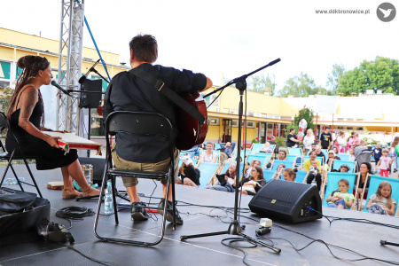 Kolorowe zdjęcie. Na scenie siedzi wokalistka Sylvetta wraz z gitarzystą. Ujęcie zrobiony od tyłu sceny. W tle widać publiczność na leżakach.