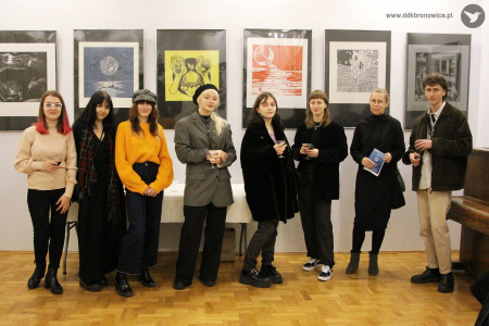 Kolorowe zdjęcie. Grupa ośmiu młodych osób pozuje na tle wystawy do zdjęcia. Są to studentki Wydziału Artystycznego z Opiekunką dr Agnieszką Zawadzką.