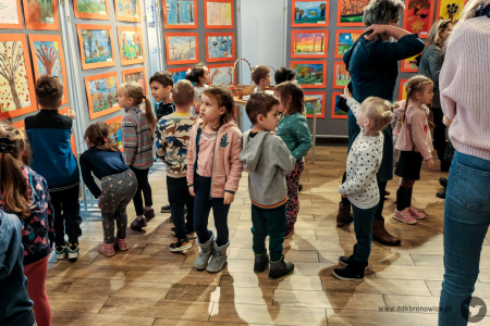 Zdjęcie kolorowe. W Galerii Małej grupa dzieci w wieku wczesnoszkolnym i nauczycielek ogląda wystawę prac.