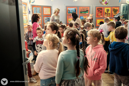 Zdjęcie kolorowe. W Galerii Małej grupa dzieci w wieku wczesnoszkolnym i nauczycielek ogląda wystawę prac.