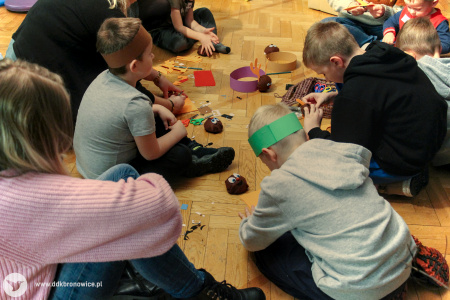 Kolorowe zdjęcie. Na podłodze siedzi trzech chłopców i wykonują pracę plastyczną - opaski zwierzęce.