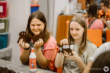 Kolorowe zdjęcie. Dwie dziewczyny pozują do zdjęcia, trzymając w dłoniach wykonane z filcu pieski.
