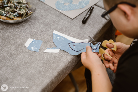 Kolorowe zdjęcie. Dziecięce dłonie wycinają kształt ryby z materiału.