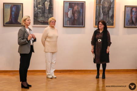 Zdjęcie. Po lewej stronie kurator wystawy przedstawia artystkę. Po środku stoi autorka wystawy. Po prawej stronie stoi kobieta. W tle wiszą obrazy.