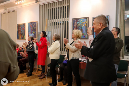 Zdjęcie. Zadowoleni uczestnicy wystawy skierowani w jednym kierunku gromko oklaskują wystąpienie artystki.