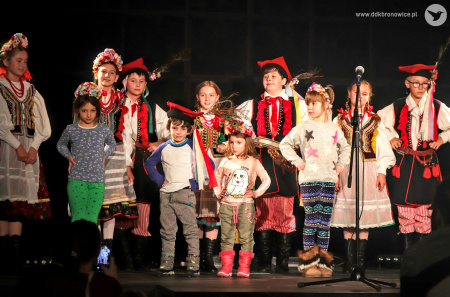 Zdjęcie kolorowe. Dzieci w strojach ludowych oraz dzieci z publiczności z ludowymi nakryciami głowy pozują na scenie do zdjęcia.