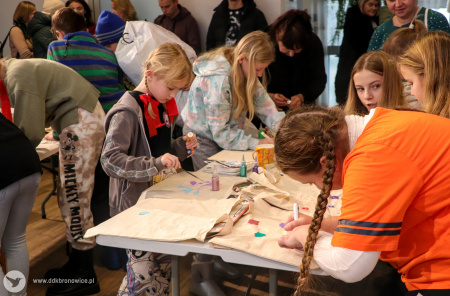Zdjęcie kolorowe. Na stole warsztatowym uczestnicy wydarzenia malują torby i odrysowują na nich wzory.