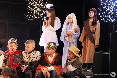 Zdjęcie. Na scenie stoją powyżej dziewczynka w przebraniu aniołka, dziewczynka w przebraniu Maryi oraz chłopiec w przebraniu Józefa. Poniżej siedzą chłopcy w strojach króli oraz pastuszków.