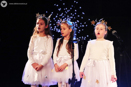 Zdjęcie. Trzy dziewczynki w białych strojach z gwiazdkowymi opaskami na głowie śpiewają.