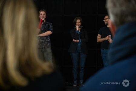 Kolorowe zdjęcie. Kobieta i dwóch mężczyzn na scenie opowiadają o projekcie. Kadr zza dwóch osób z publiczności.