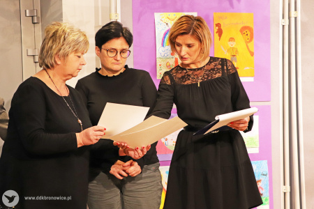 Zdjęcie. Trzy kobiety. W dłoniach trzymają wspólnie dyplomy. Spoglądają na nie.