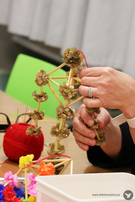 Zdjęcie. Ręce uczestniczki, która ozdabia kryształek bibułą. Na stole leżą nożyczki, kordonek i materiały do wykonania ozdób.