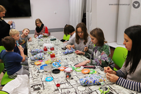 Zdjęcie. Grupa dzieci siedzi przy stole i zszywa pluszowe aniołki.