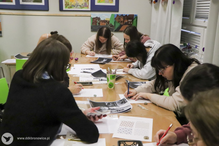 Kolorowe zdjęcie. Grupa uczestniczek warsztatów siedzi przy stole. Szkicują ołówkami na kartkach.