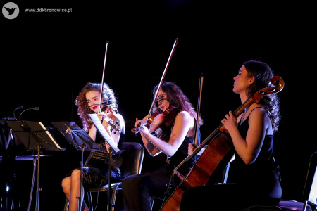 Zdjęcie. Trzy kobiety akompaniamentujące podczas koncertu. Dwie grają na skrzypcach, jedna na wiolonczeli.