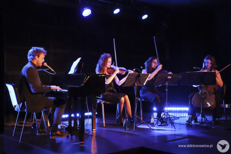 Zdjęcie. Na scenie Janek Traczyk gra na fortepianie i śpiewa, akompaniamentują mu dwie skrzypaczki i wiolonczelistka.