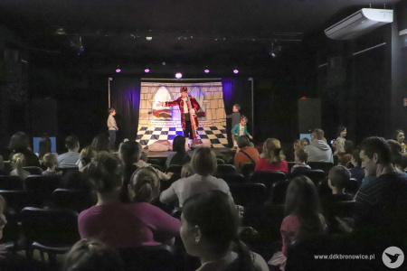 Zdjęcie. Publiczność oglądająca spektakl. w tle na scenie aktor oraz trójka dzieci.