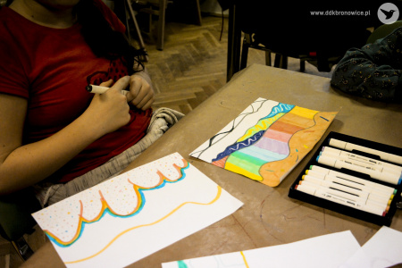 Kolorowe zdjęcie. Dziewczynka przy stoliku rysuje flamastrami na białej kartce.