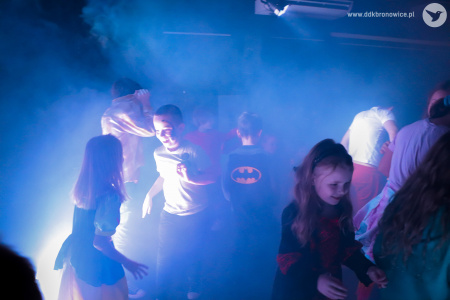 Kolorowe zdjęcie. Grupa dzieci w przebraniach tańczy na zaciemnionej sali wśród dymu scenicznego.